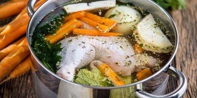 不锈钢锅装满鸡腿，胡萝卜，洋葱和新鲜香草和水.